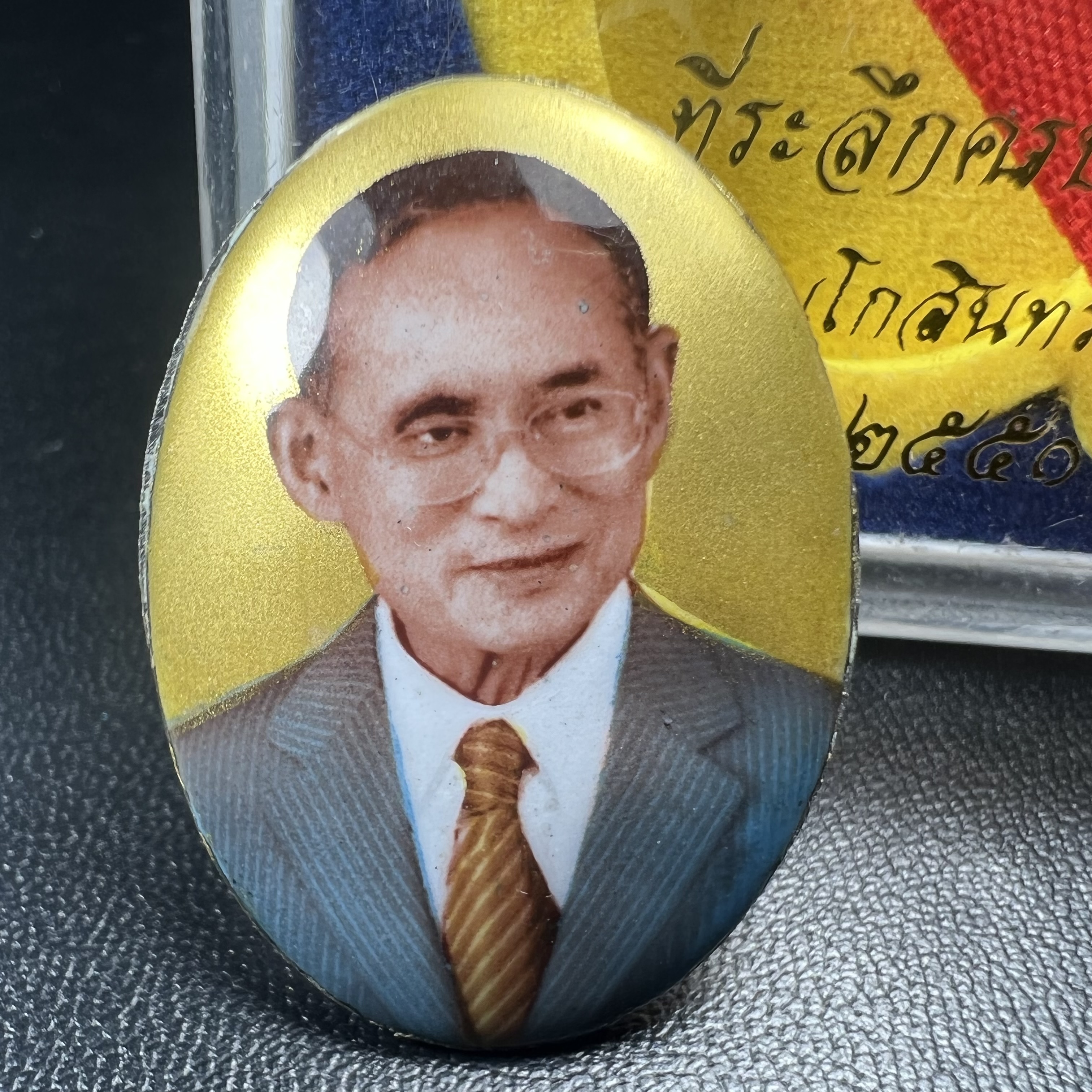 ล็อกเกตในหลวงรัชกาลที่9 ที่ระลึกครบ 25 ปี มูลนิธิศรีรัตนโกสินทร์ วัดสุทธาราม พ.ศ. 2550 พิมพ์ทรงวงรีรูปไข่เล็กฉากสีทอง หลังปิดแผ่นโลหะสีขาว(สแตนเลส)ฝังพระยอดธง(นิยม)