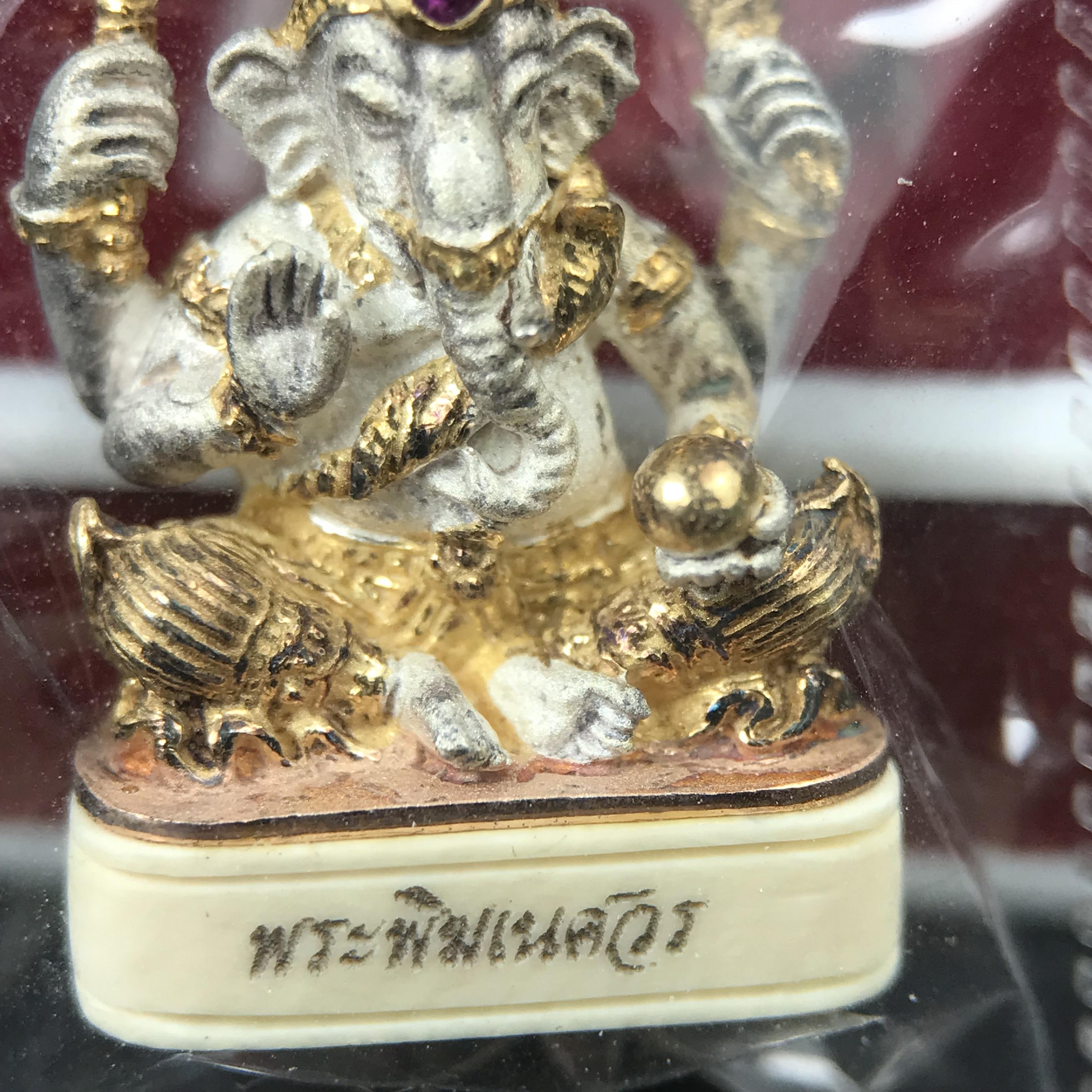 พระพิฆเนศวร รุ่น คชสารหมื่นปี รูปเหมือนพระพิฆเนศวรนั่งประทานพรฐานงาช้างแมมมอสขนาดห้อยคอ เนื้อเงินชุบสามกษัตริย์ขัดเงา พิมพ์เล็ก สูง 2.2 ซม. ฝังพลอยทับทิมแท้ พิธีมหาเทวาภิเษก ณ. เทวสถานโบสถ์พราหมณ์ (เสาชิงช้า) โดยเกจิคณาจารย์ทั่วประทศ ปี 2545(หมายเลข ๓๐)