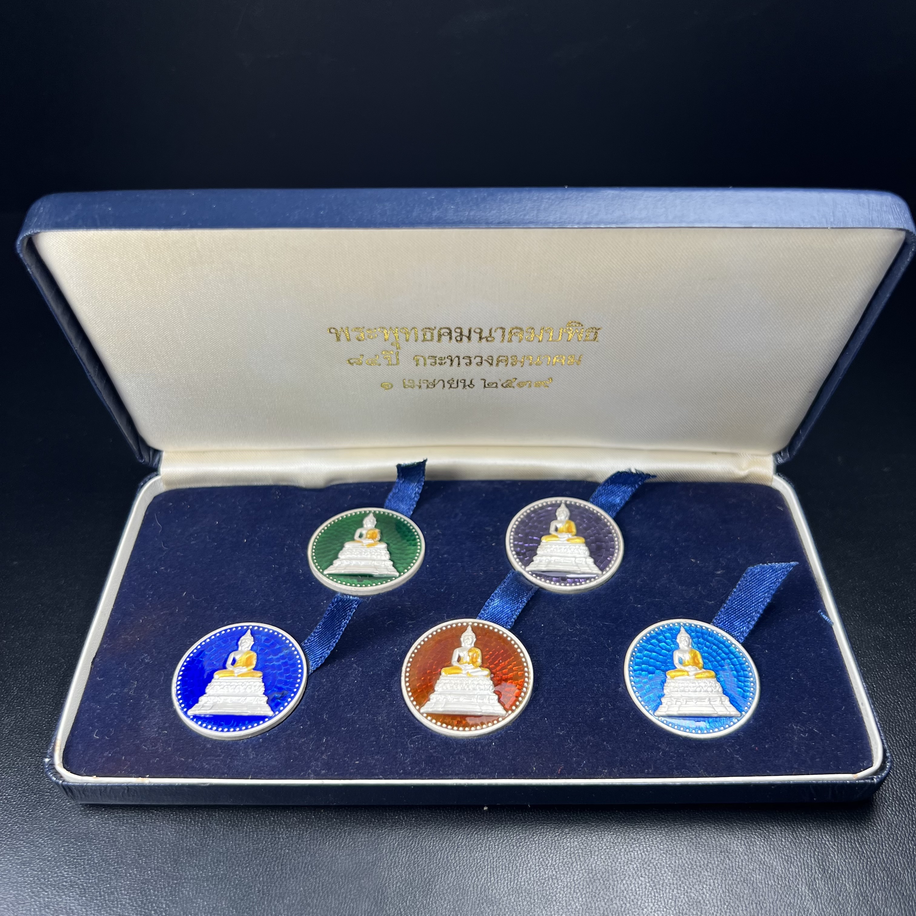 พระพุทธคมนาคมบพิธ (พระพุทธสิหิงค์จำลอง)(พระพุทธรูปประจำกระทรวงคมนาคม) หลังตรา ภปร. ครบรอบ 84 ปี กระทรวงคมนาคม พ.ศ.2539 ชุดเหรียญเนื้อเงินลงยา ขนาด 2.8 ซม. ครบชุดห้าสีพร้อมกล่องบรรจุเดิม ปลุกเสก ณ วัดพระแก้ว พิธีใหญ่