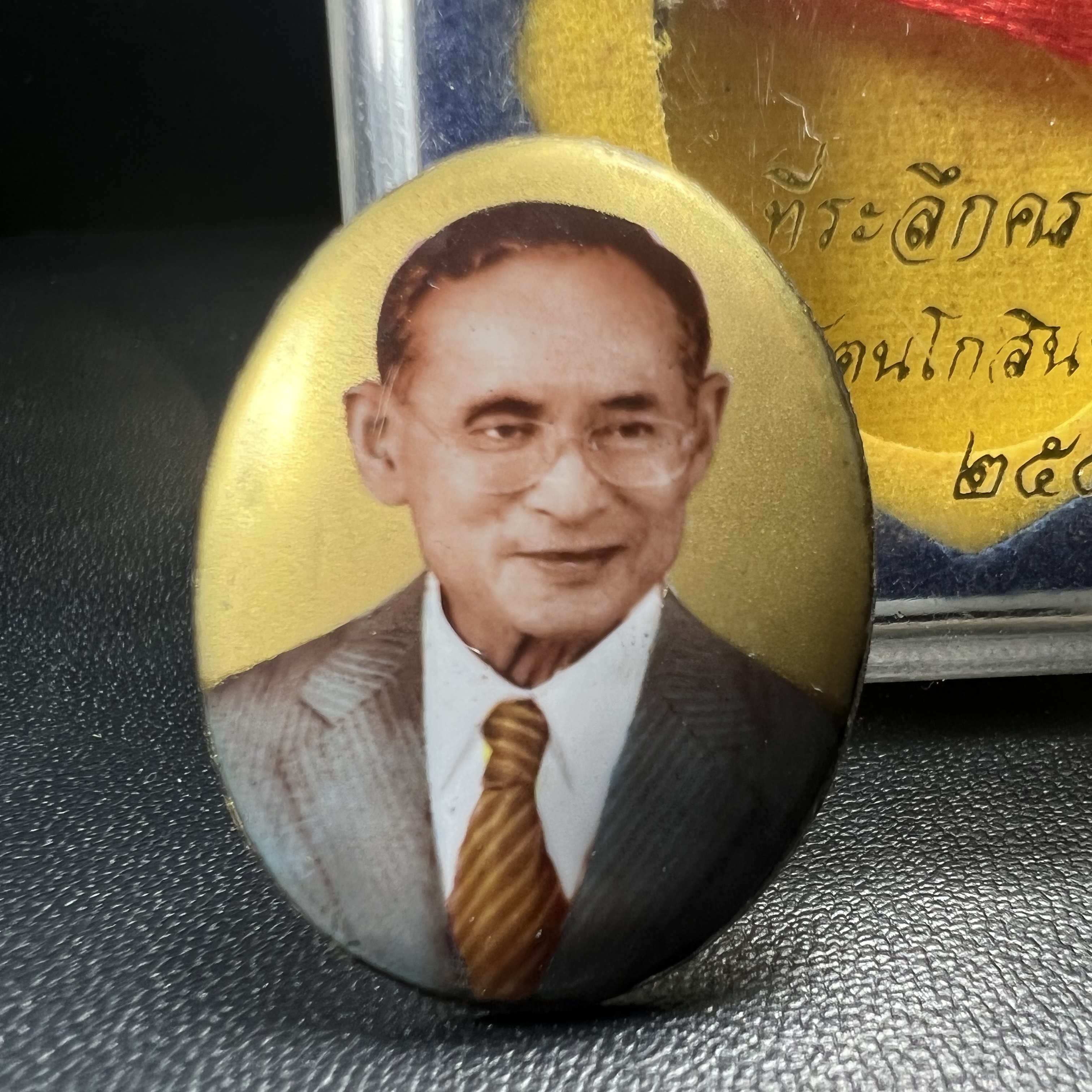 ล็อกเกตในหลวงรัชกาลที่9 ที่ระลึกครบ 25 ปี มูลนิธิศรีรัตนโกสินทร์ วัดสุทธาราม พ.ศ. 2550 พิมพ์ทรงวงรีรูปไข่เล็กฉากสีทอง หลังปิดแผ่นโลหะสีขาว(สแตนเลส)ฝังพระยอดธง(นิยม)