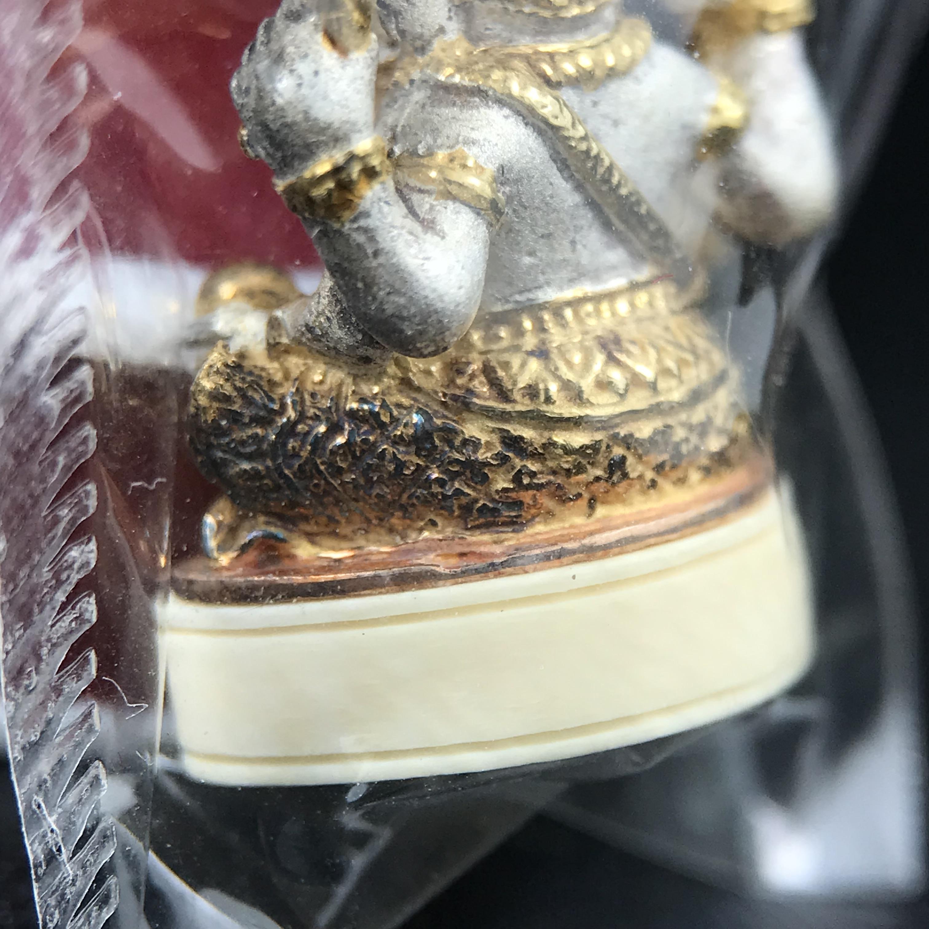 พระพิฆเนศวร รุ่น คชสารหมื่นปี รูปเหมือนพระพิฆเนศวรนั่งประทานพรฐานงาช้างแมมมอสขนาดห้อยคอ เนื้อเงินชุบสามกษัตริย์ขัดเงา พิมพ์เล็ก สูง 2.2 ซม. ฝังพลอยทับทิมแท้ พิธีมหาเทวาภิเษก ณ. เทวสถานโบสถ์พราหมณ์ (เสาชิงช้า) โดยเกจิคณาจารย์ทั่วประทศ ปี 2545(หมายเลข ๓๐)
